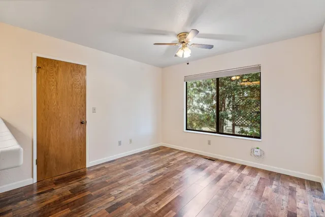an empty room with wooden floor fan and windows