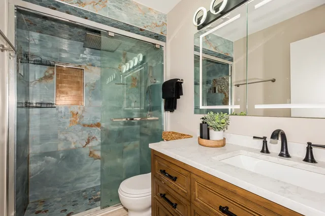 a bathroom with a granite countertop sink a toilet a mirror and shower