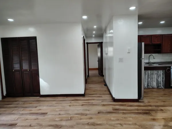 an empty room with wooden floor and a kitchen