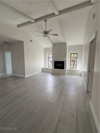 an empty room with wooden floor fireplace and windows