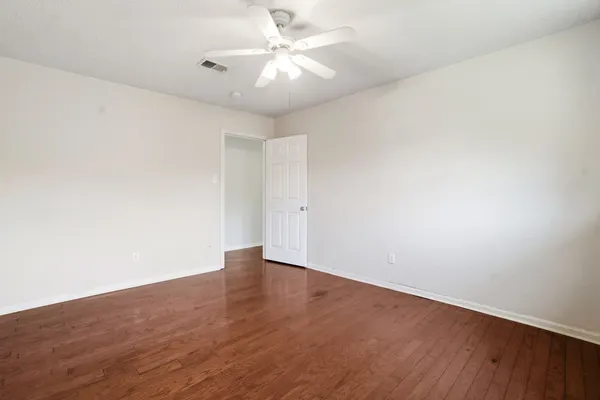 an empty room with wooden floor and fan chandelier