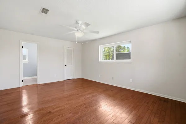 an empty room with wooden floor chandelier fan and windows