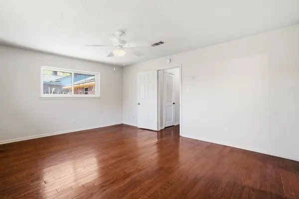 an empty room with wooden floor ceiling fan and windows