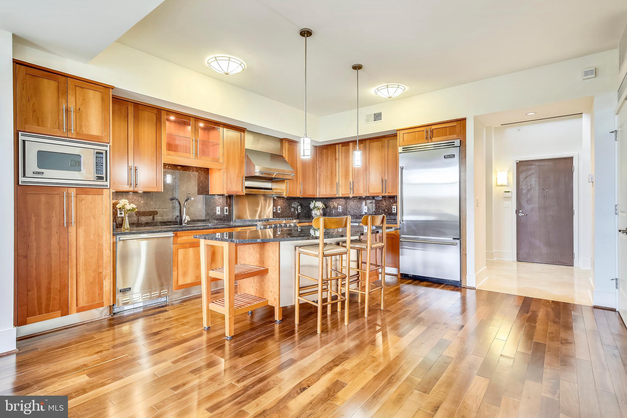4301 Military Road Northwest, Unit PH5 Washington, DC 20015 - Photo 7 of 53 a kitchen with stainless steel appliances granite countertop a refrigerator a stove top oven and a dining table with wooden floor