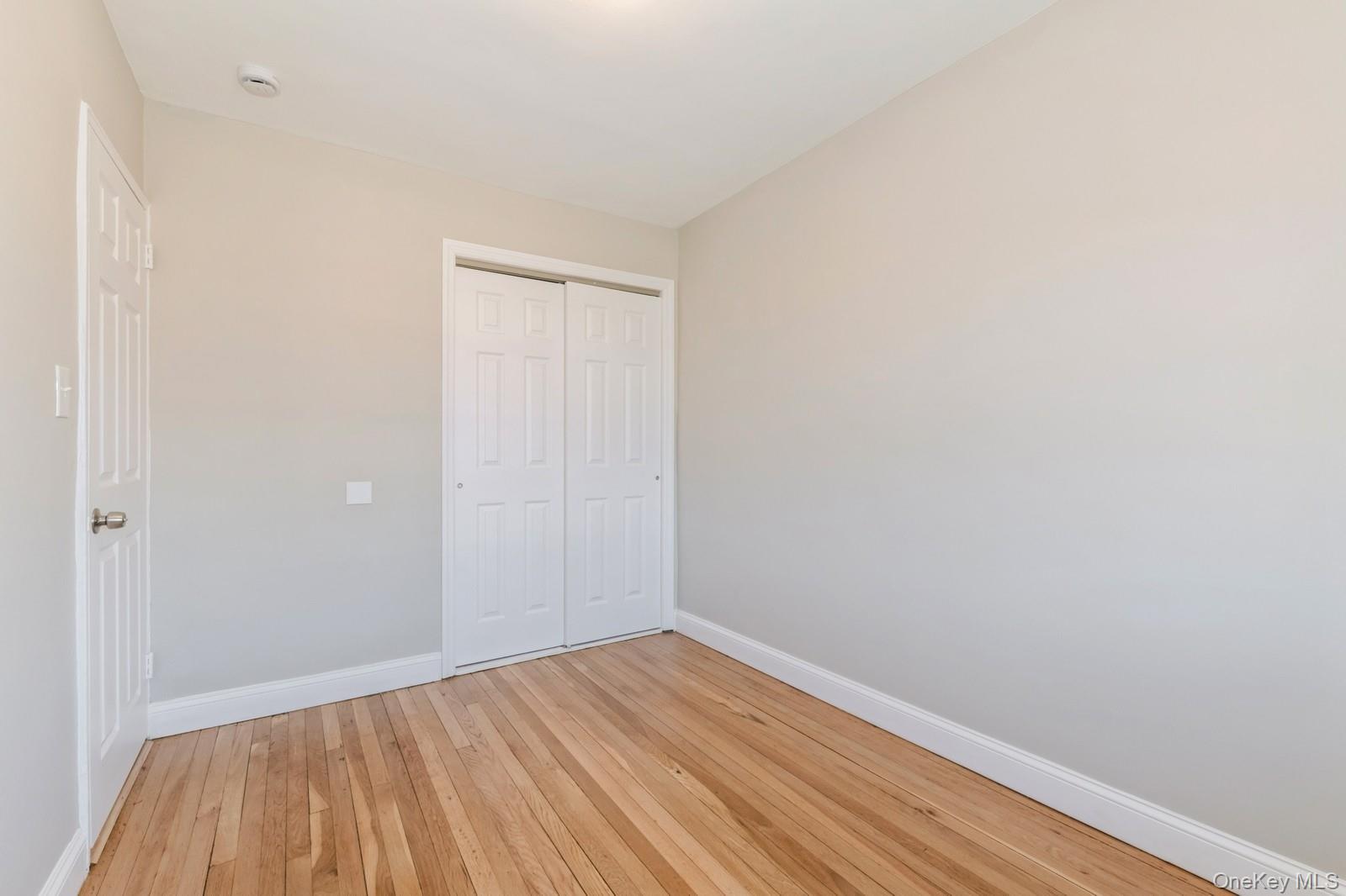 74-67 220th Street, Unit 101A Queens, NY 11364 - Photo 11 of 15 Unfurnished bedroom featuring a closet, light wood-style flooring, and baseboards