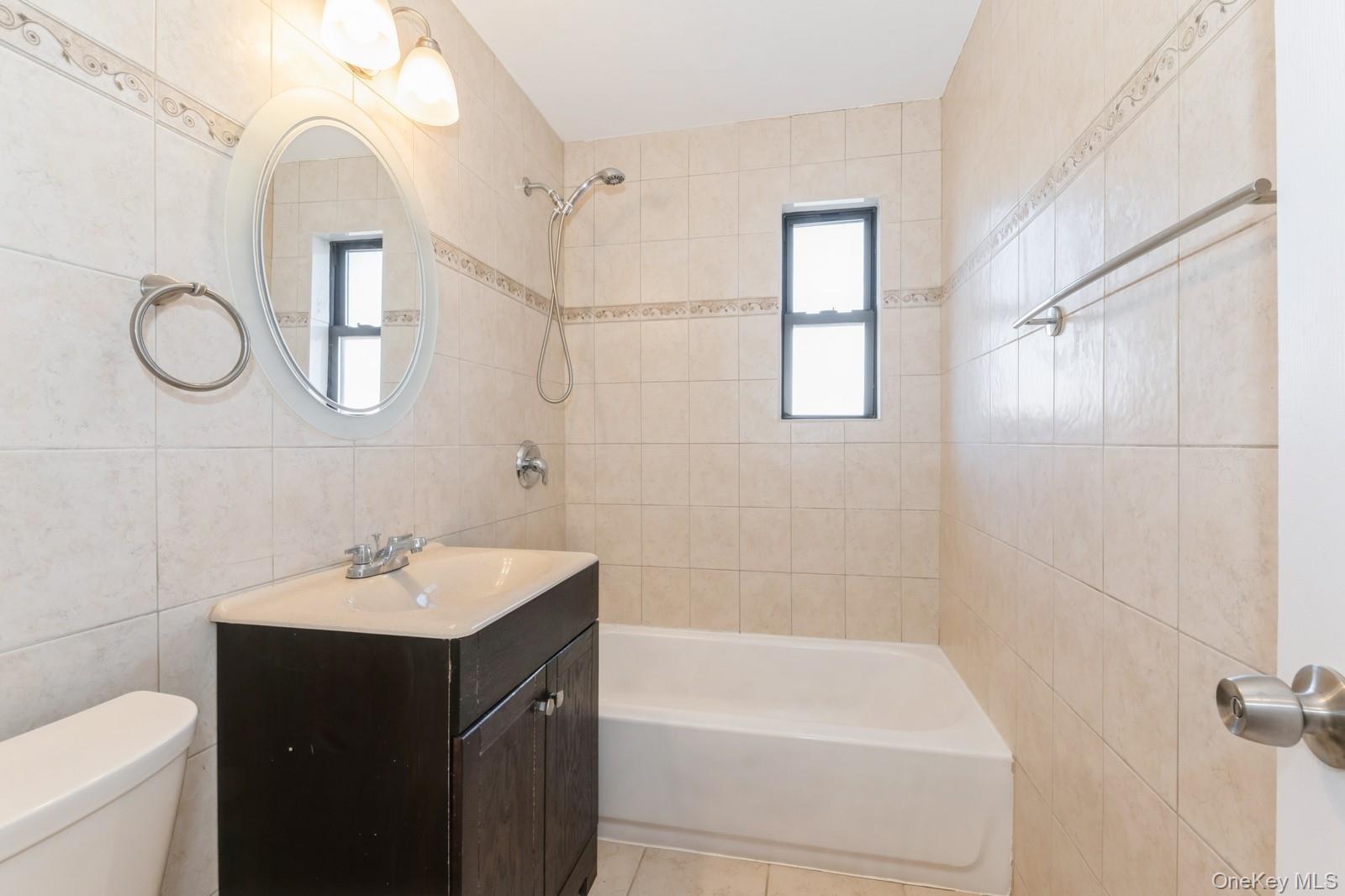 74-67 220th Street, Unit 101A Queens, NY 11364 - Photo 12 of 15 Bathroom featuring tile walls, bathing tub / shower combination, a healthy amount of sunlight, and toilet