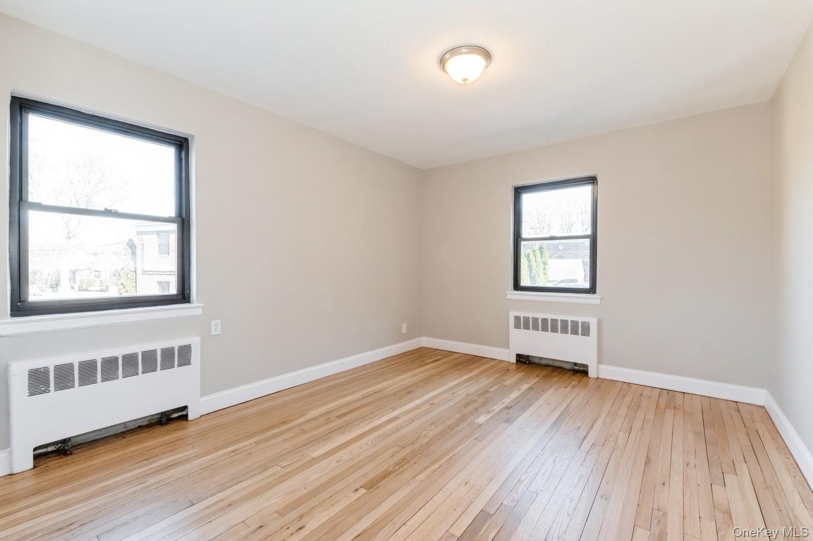 74-67 220th Street, Unit 101A Queens, NY 11364 - Photo 13 of 15 Unfurnished room featuring baseboards, radiator heating unit, and light wood finished floors