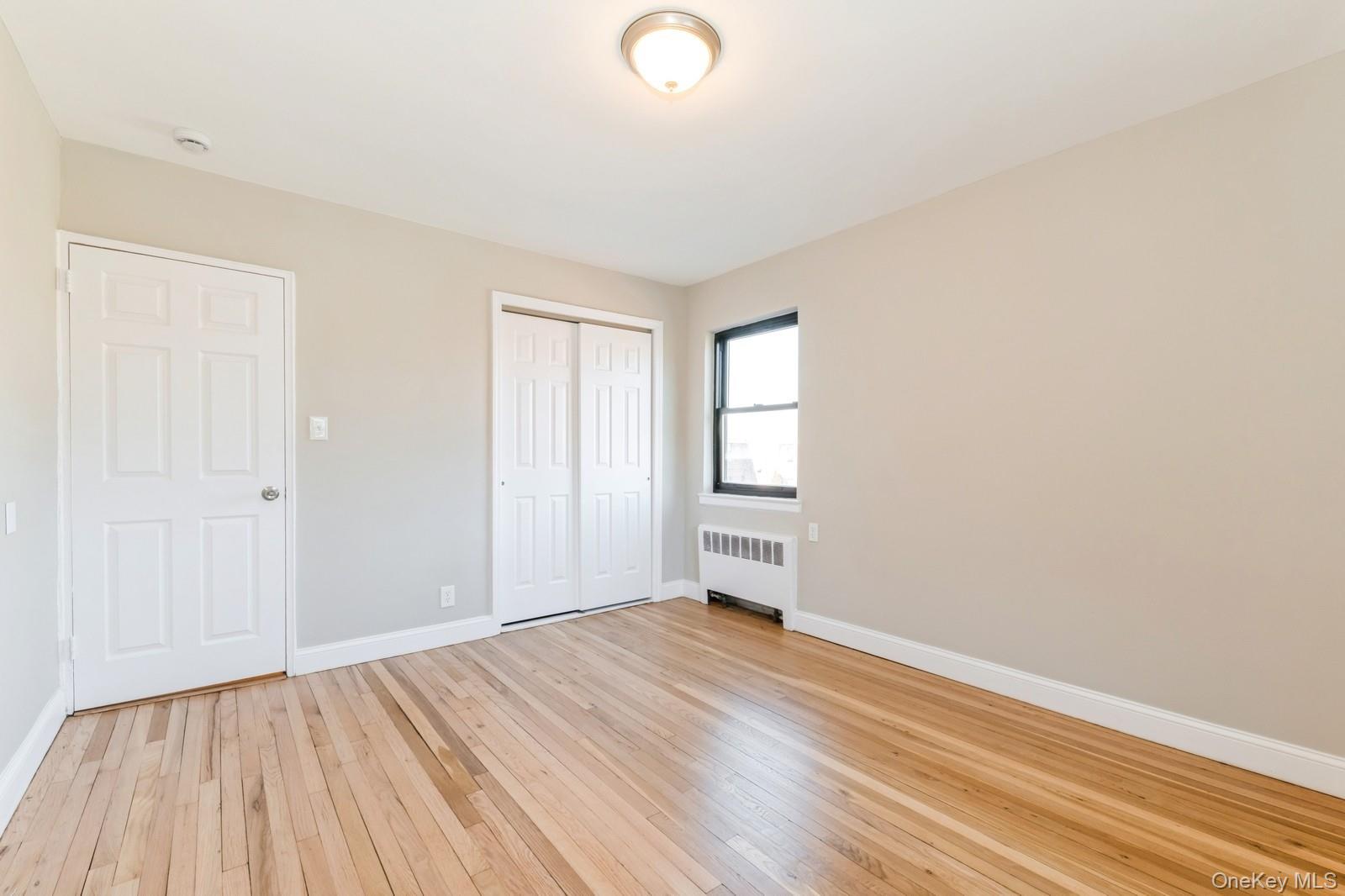 74-67 220th Street, Unit 101A Queens, NY 11364 - Photo 15 of 15 Unfurnished bedroom featuring a closet, light wood-style flooring, radiator heating unit, and baseboards