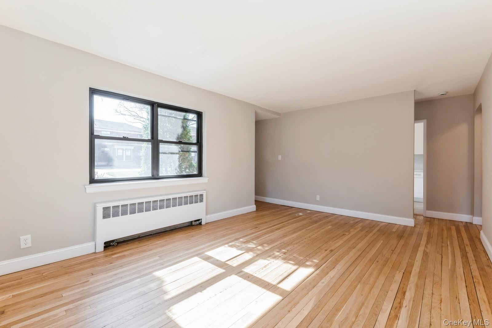 74-67 220th Street, Unit 101A Queens, NY 11364 - Photo 6 of 15 Spare room featuring radiator, light wood-type flooring, and baseboards