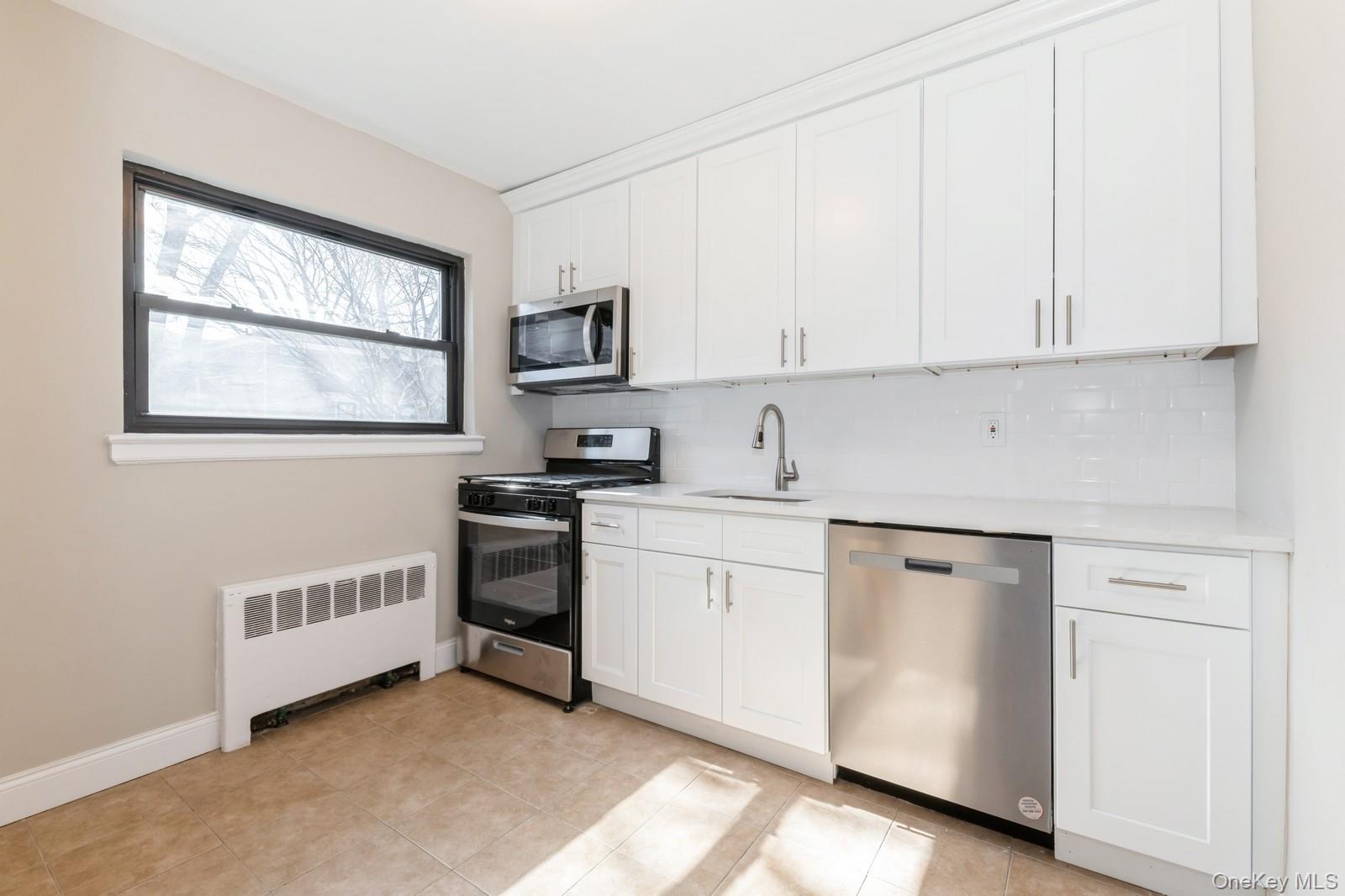 74-67 220th Street, Unit 101A Queens, NY 11364 - Photo 7 of 15 Kitchen featuring a sink, tasteful backsplash, radiator heating unit, stainless steel appliances, and light countertops