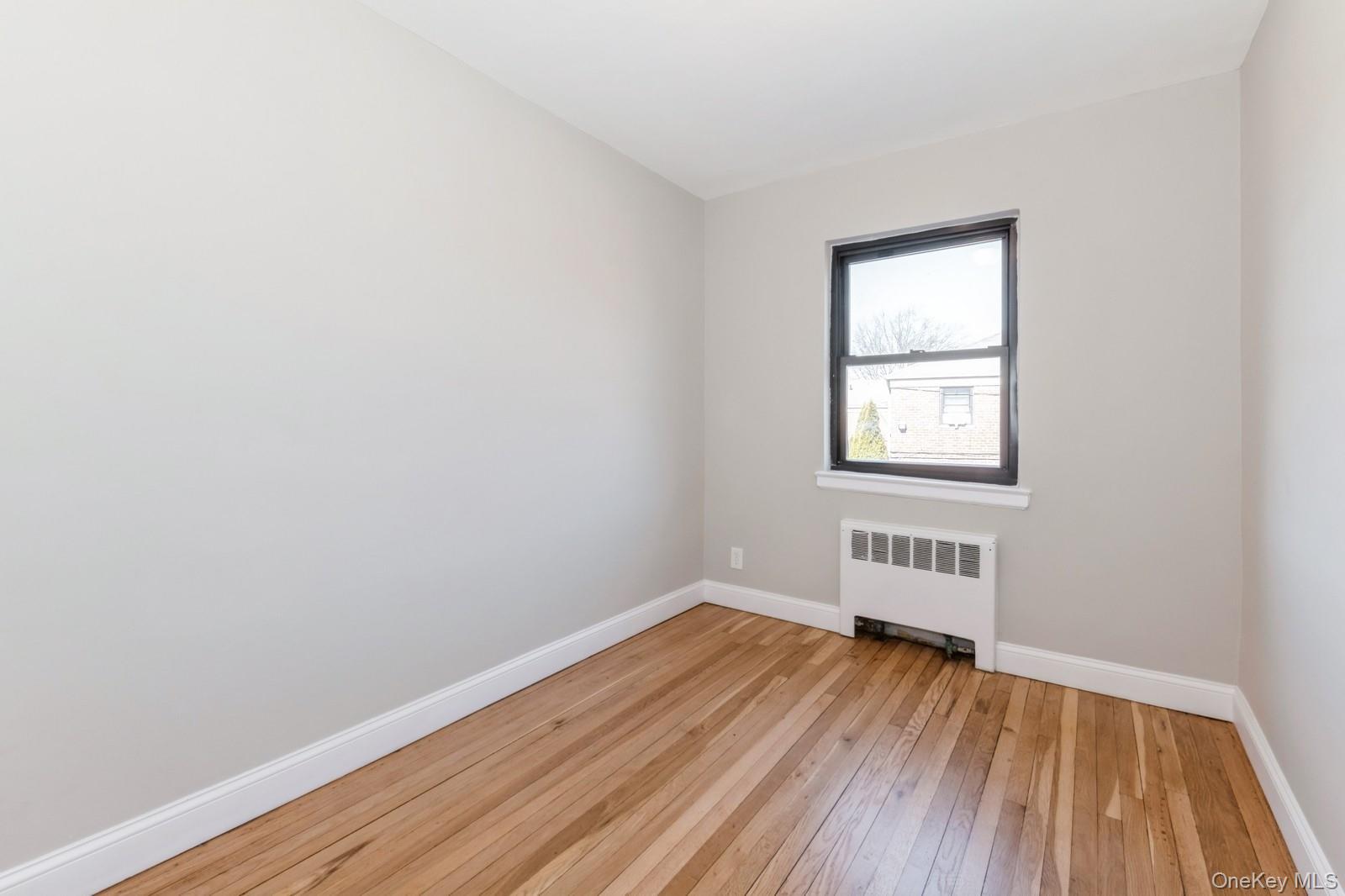 74-67 220th Street, Unit 101A Queens, NY 11364 - Photo 9 of 15 Spare room featuring light wood-style floors, baseboards, and radiator
