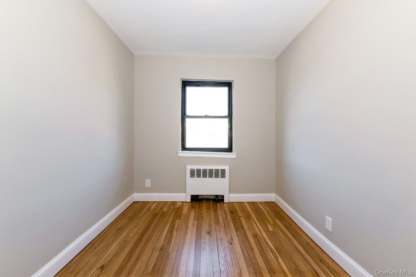 74-67 220th Street, Unit 101A Queens, NY 11364 - Photo 10 of 15 Empty room featuring light wood-type flooring, baseboards, and radiator