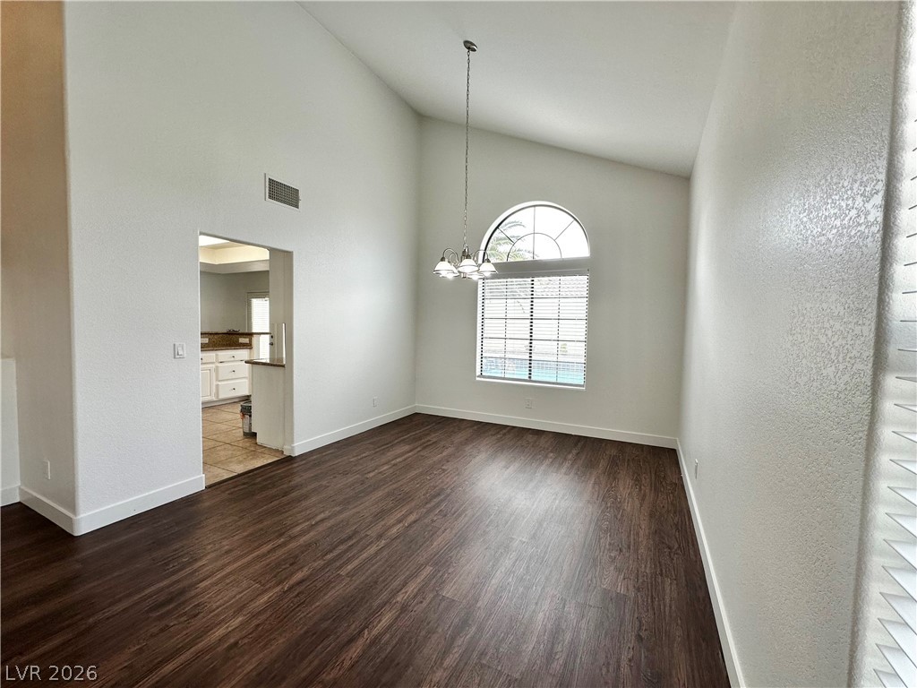 2113 Rico Peak Court Las Vegas, NV 89128 - Photo 16 of 53 Unfurnished dining area with dark wood-type flooring, lofted ceiling, hanging lights, and a textured wall
