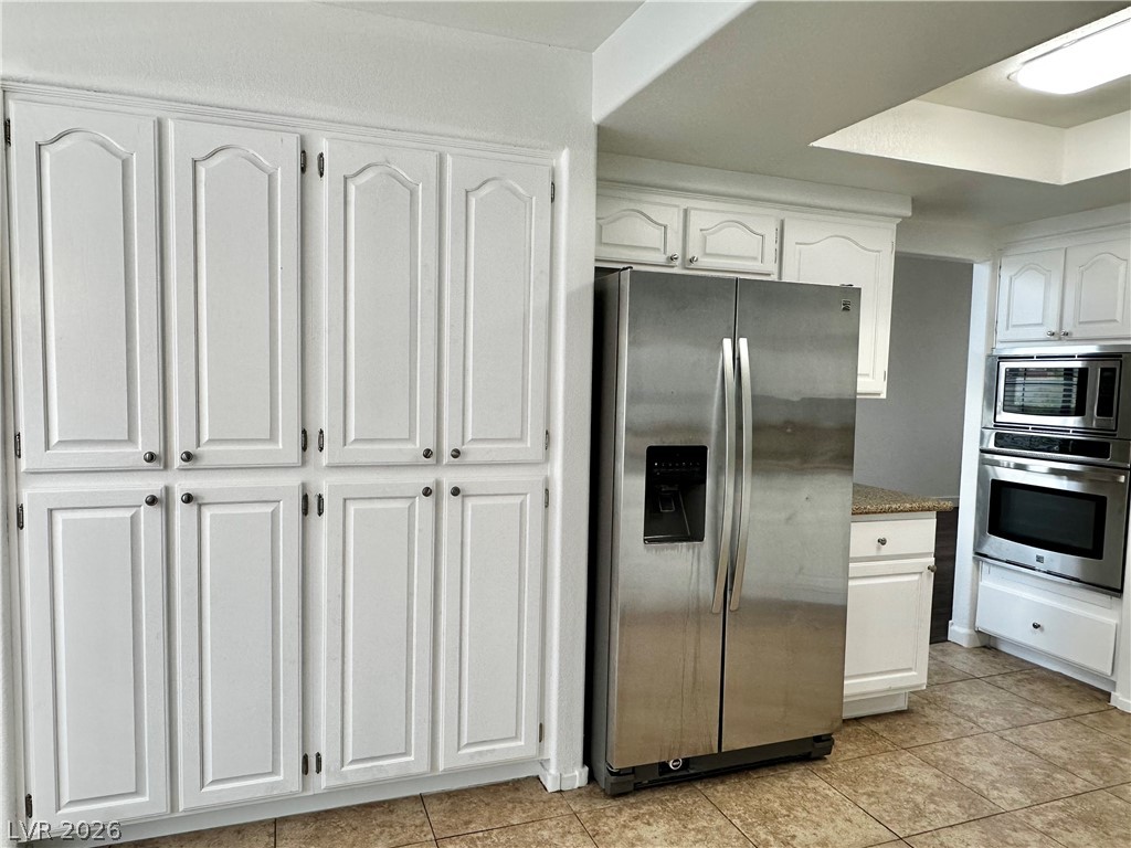 2113 Rico Peak Court Las Vegas, NV 89128 - Photo 25 of 53 Kitchen featuring white cabinets, stainless steel appliances, light tile patterned floors, and dark stone countertops
