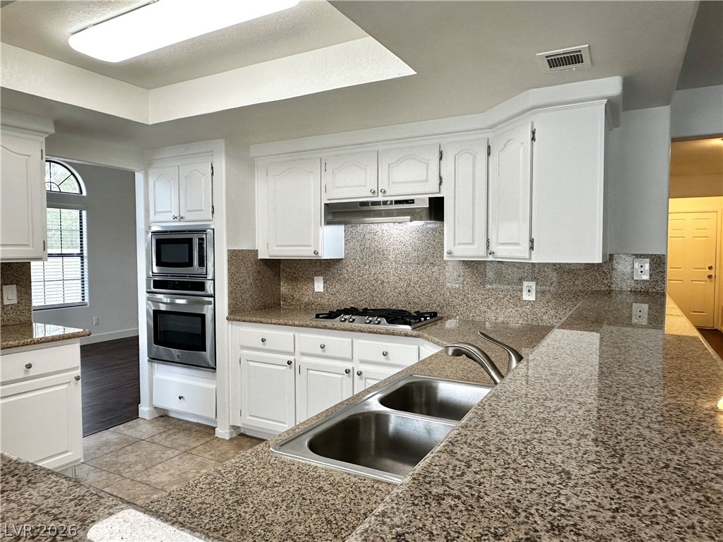 2113 Rico Peak Court Las Vegas, NV 89128 - Photo 26 of 53 Kitchen with white cabinets, backsplash, stainless steel appliances, a tray ceiling, and light tile patterned flooring