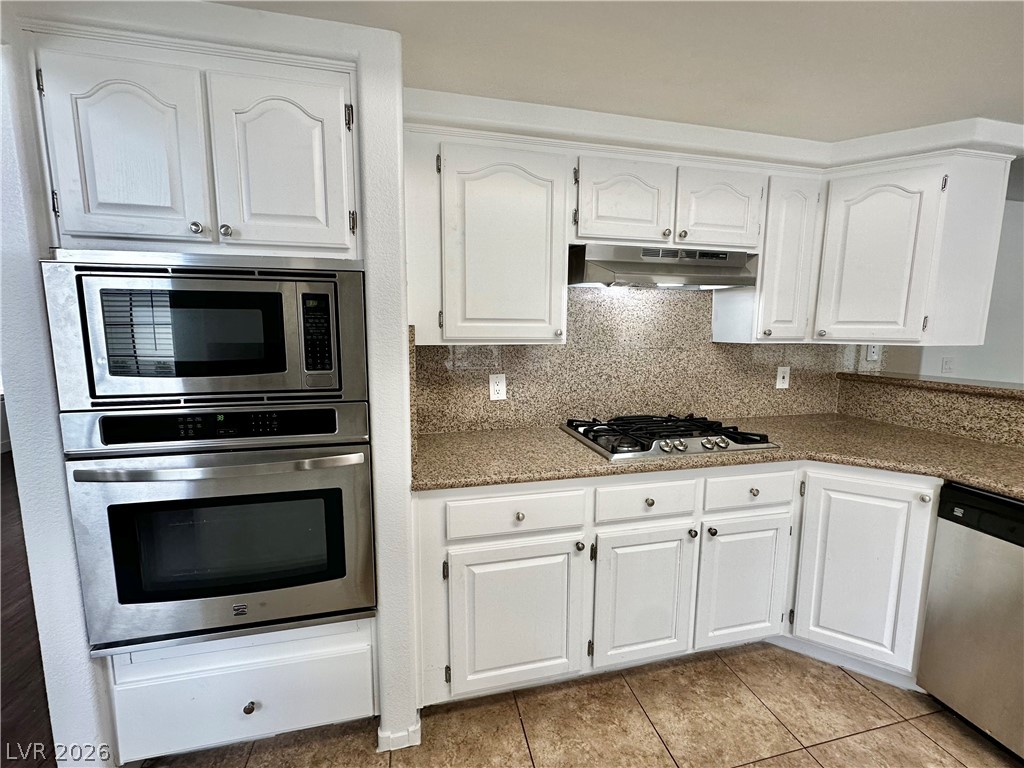 2113 Rico Peak Court Las Vegas, NV 89128 - Photo 5 of 53 Kitchen with white cabinetry, backsplash, stainless steel appliances, light tile patterned floors, and light stone countertops