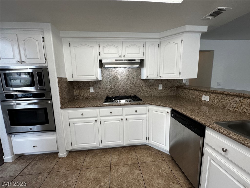 2113 Rico Peak Court Las Vegas, NV 89128 - Photo 7 of 53 Kitchen with white cabinetry, stainless steel appliances, backsplash, dark tile patterned floors, and dark stone counters