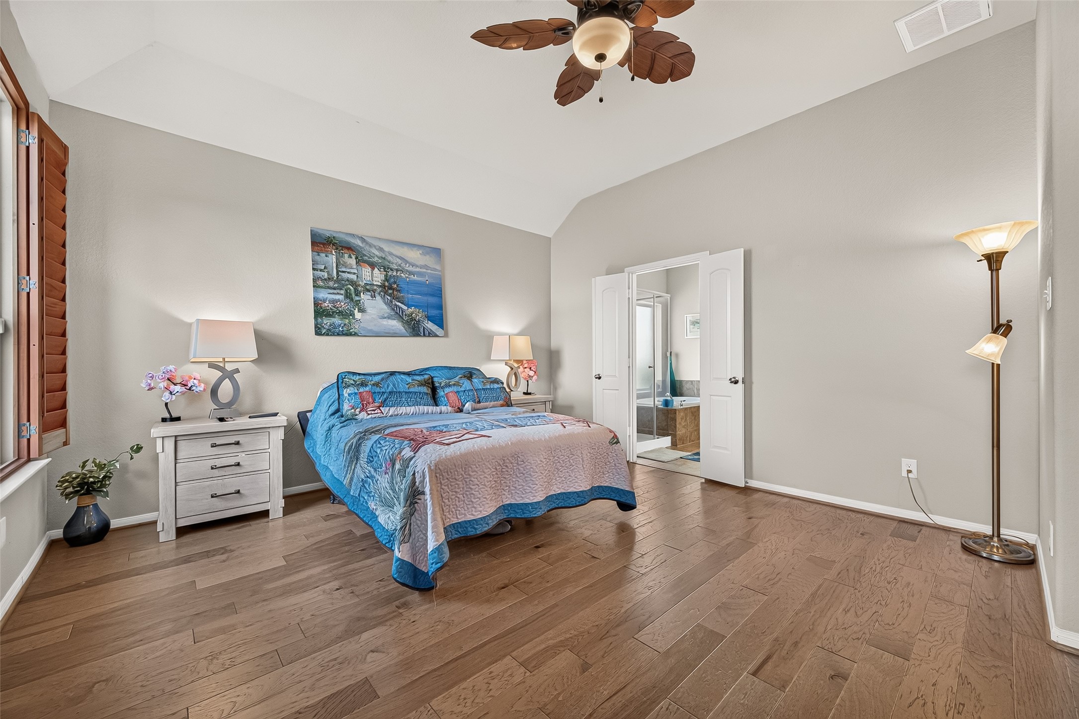 4910 Culver Lane Rosenberg, TX 77471 - Photo 34 of 50 Primary bedroom features a ceiling fan with a leaf design and light fixture. Natural light filters through wooden shutters, and double doors lead to an en-suite bathroom.