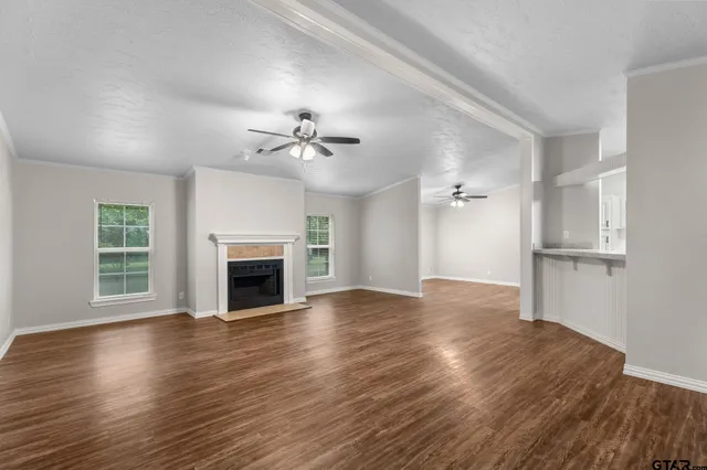 a view of an empty room with wooden floor fireplace and a window
