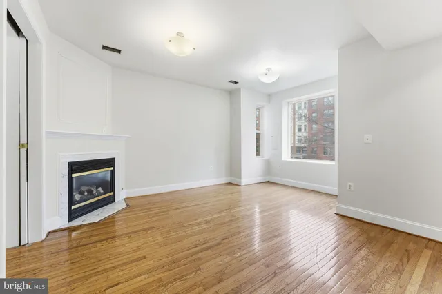 a view of an empty room with wooden floor fireplace and a window