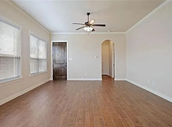 an empty room with wooden floor chandelier fan and windows