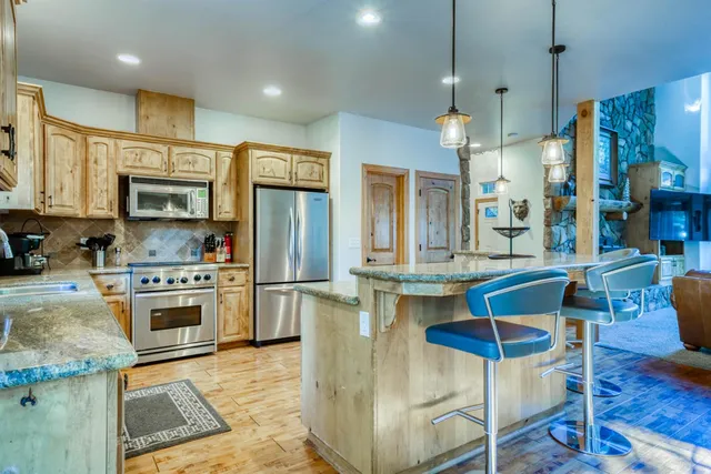 a kitchen with stainless steel appliances granite countertop a kitchen island a stove a sink a dining table and chairs with wooden floor