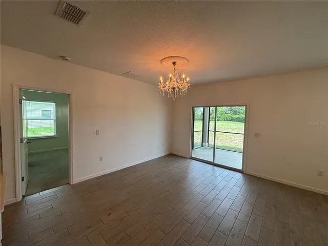 an empty room with wooden floor chandelier and windows