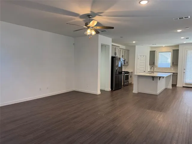 a view of an empty room with wooden floor and a ceiling fan