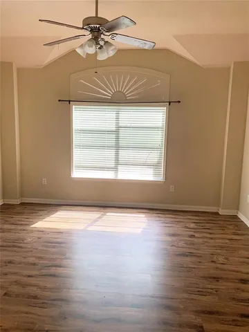 an empty room with wooden floor fan and windows