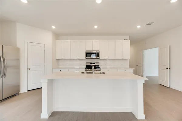 a kitchen with stainless steel appliances a refrigerator sink stove and white cabinets