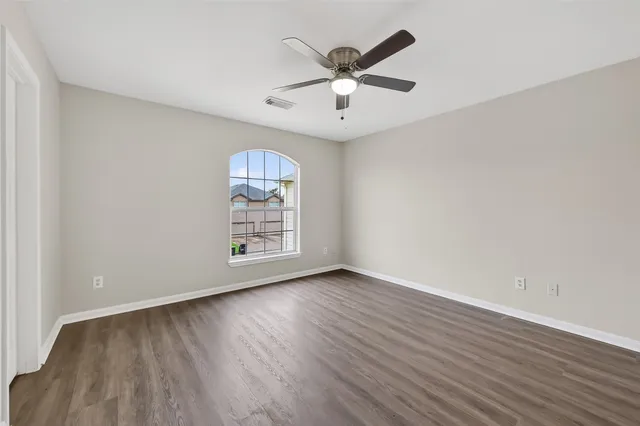an empty room with wooden floor chandelier fan and windows
