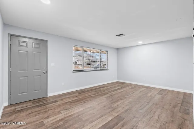a view of an empty room with wooden floor and a window
