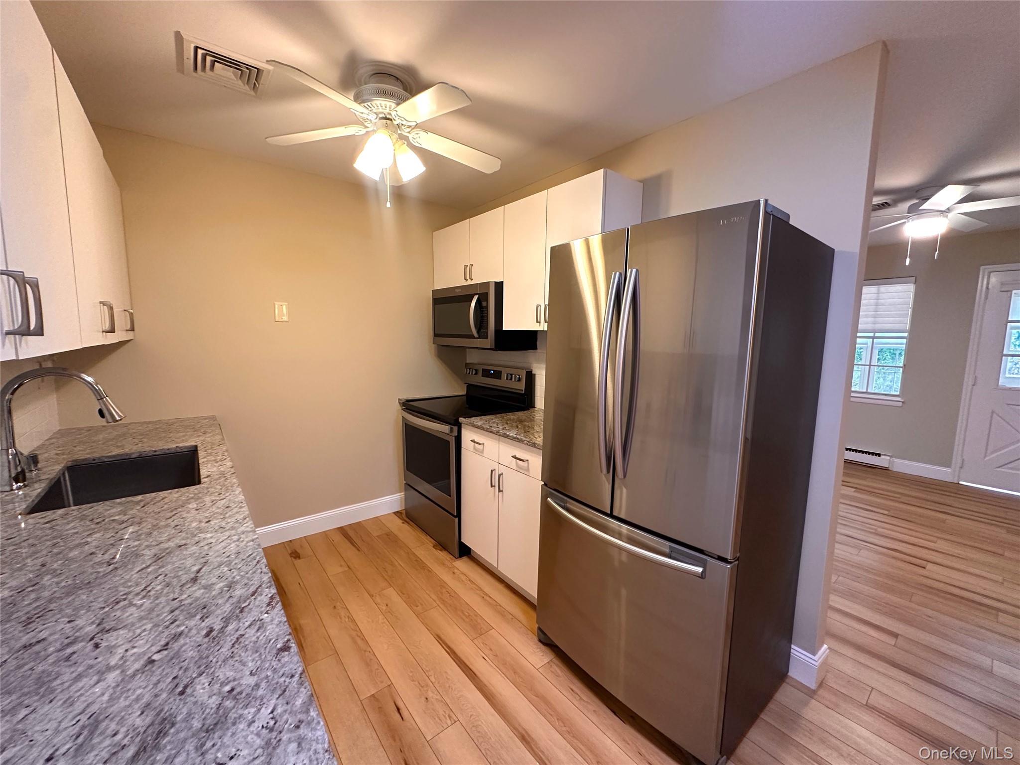 312 Woodbridge Drive, Unit C Ridge, NY 11961 - Photo 7 of 12 a kitchen with stainless steel appliances a refrigerator a sink a stove and a refrigerator with wooden floor