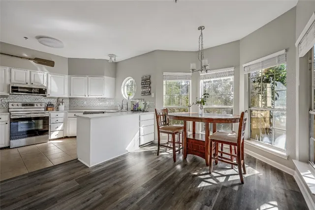 a kitchen with stainless steel appliances granite countertop a stove a refrigerator a kitchen island a table and chairs with wooden floor