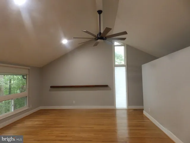 an empty room with wooden floor fan and windows