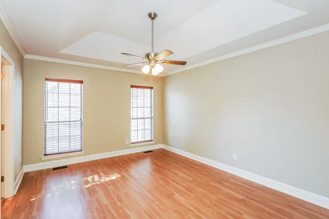 an empty room with wooden floor chandelier fan and windows