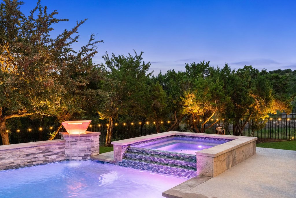 215 Lodestone Lane Austin, TX 78738 - Photo 37 of 40 An illuminated backyard oasis featuring a shimmering pool, an inviting spa, and twinkling lights for evening ambiance.