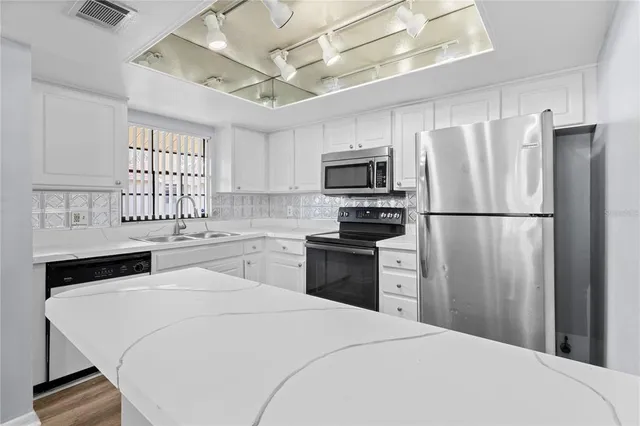 a kitchen with granite countertop a refrigerator a sink dishwasher a stove top oven a refrigerator with grey cabinets and wooden floor