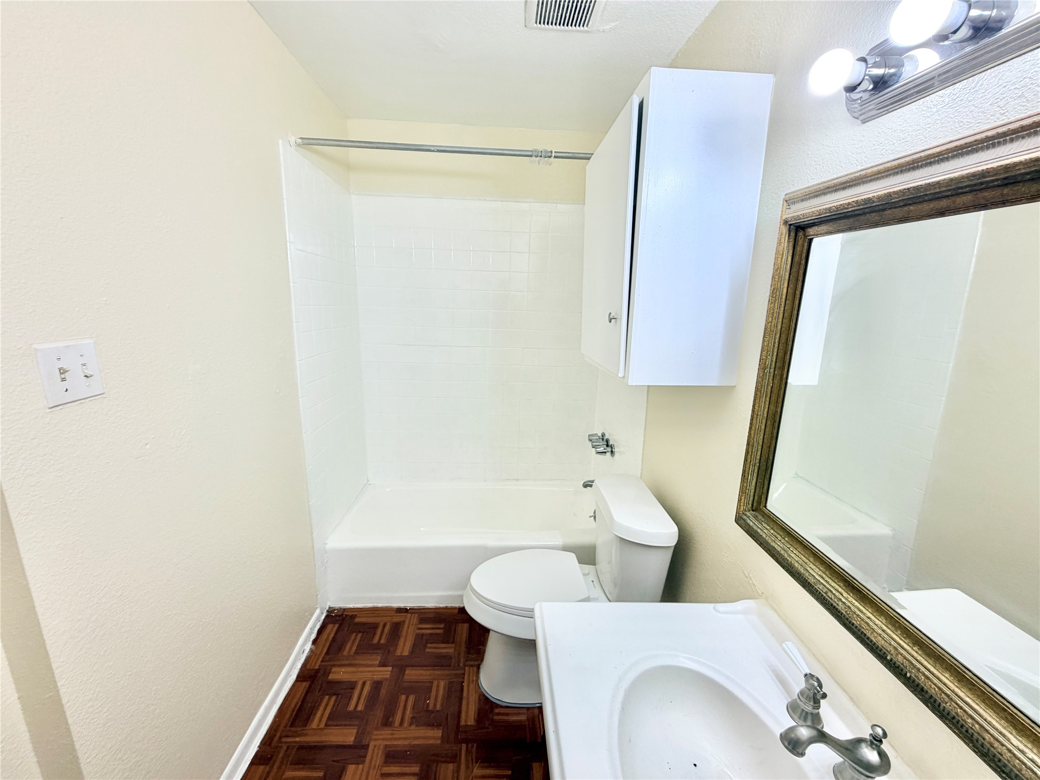 6257 Manor Road, Unit B Austin, TX 78723 - Photo 26 of 38 Bathroom featuring wood-finish parquet flooring, a white vanity with integrated sink, a large framed mirror, and a white tiled shower-tub combination