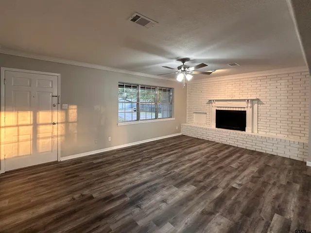 an empty room with wooden floor fireplace and windows