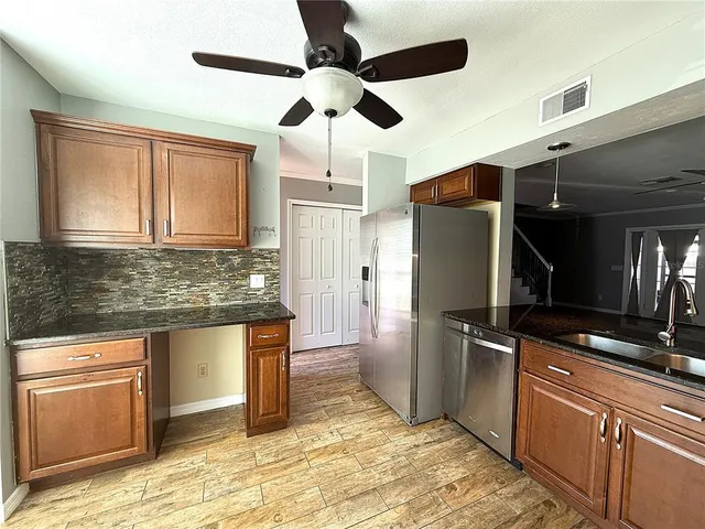 a kitchen with stainless steel appliances granite countertop a refrigerator a stove and a sink with wooden floors