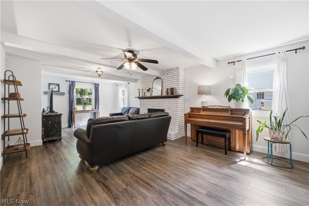 2411 Ridgeview Lane Youngstown, OH 44514 - Photo 12 of 48 Spacious living area featuring wood-finish flooring, exposed ceiling beams, a white-painted brick fireplace with a dark wood mantle, and multiple windows providing natural illumination