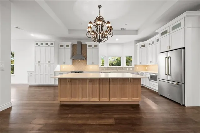 a kitchen with stainless steel appliances granite countertop a refrigerator a sink dishwasher a stove and white cabinets with wooden floor