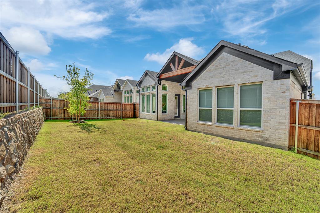 3520 Helios Lane Corinth, TX 76208 - Photo 37 of 37 Expansive grassy lawn with a young tree, bordered by a wood fence and a stone retaining wall