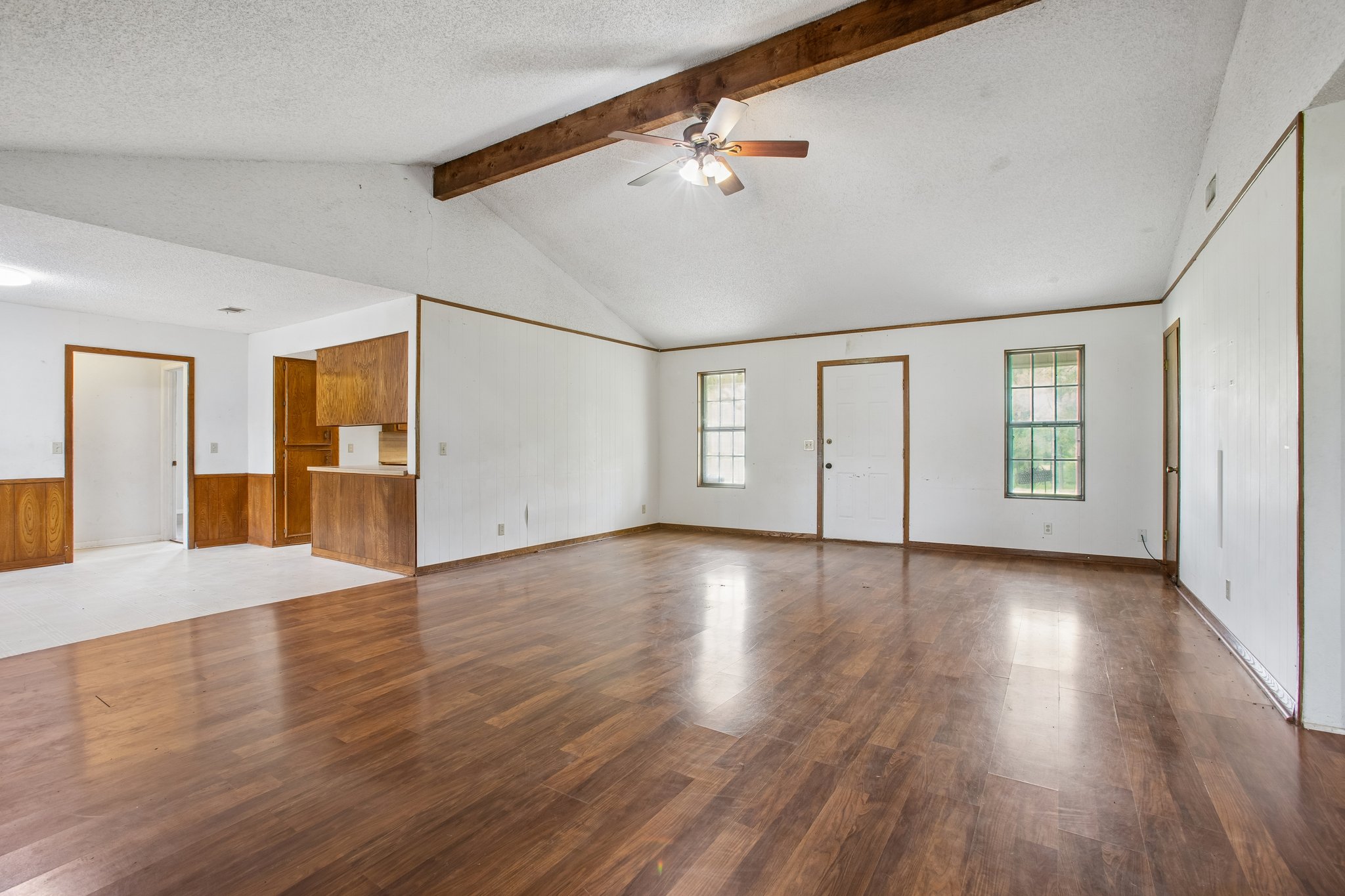 406 Monkey Road Elgin, TX 78621 - Photo 7 of 39 Spacious living area featuring wood-finish flooring, a vaulted ceiling with exposed wood beam, a ceiling fan, and white walls with wood trim accents