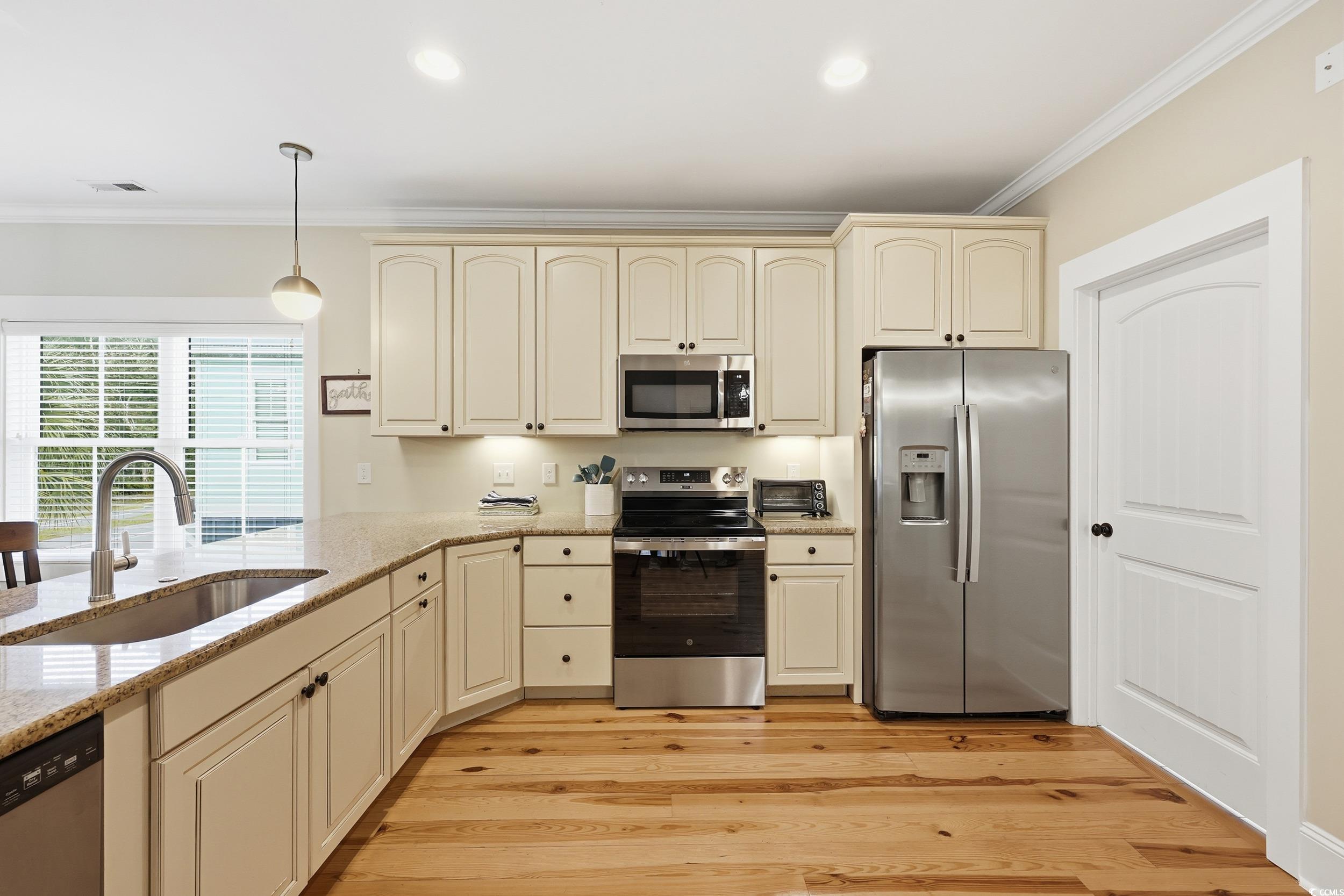 43 Sandlapper Way Pawleys Island, SC 29585 - Photo 7 of 33 Kitchen featuring cream cabinets, appliances with stainless steel finishes, ornamental molding, light stone countertops, and light wood-type flooring