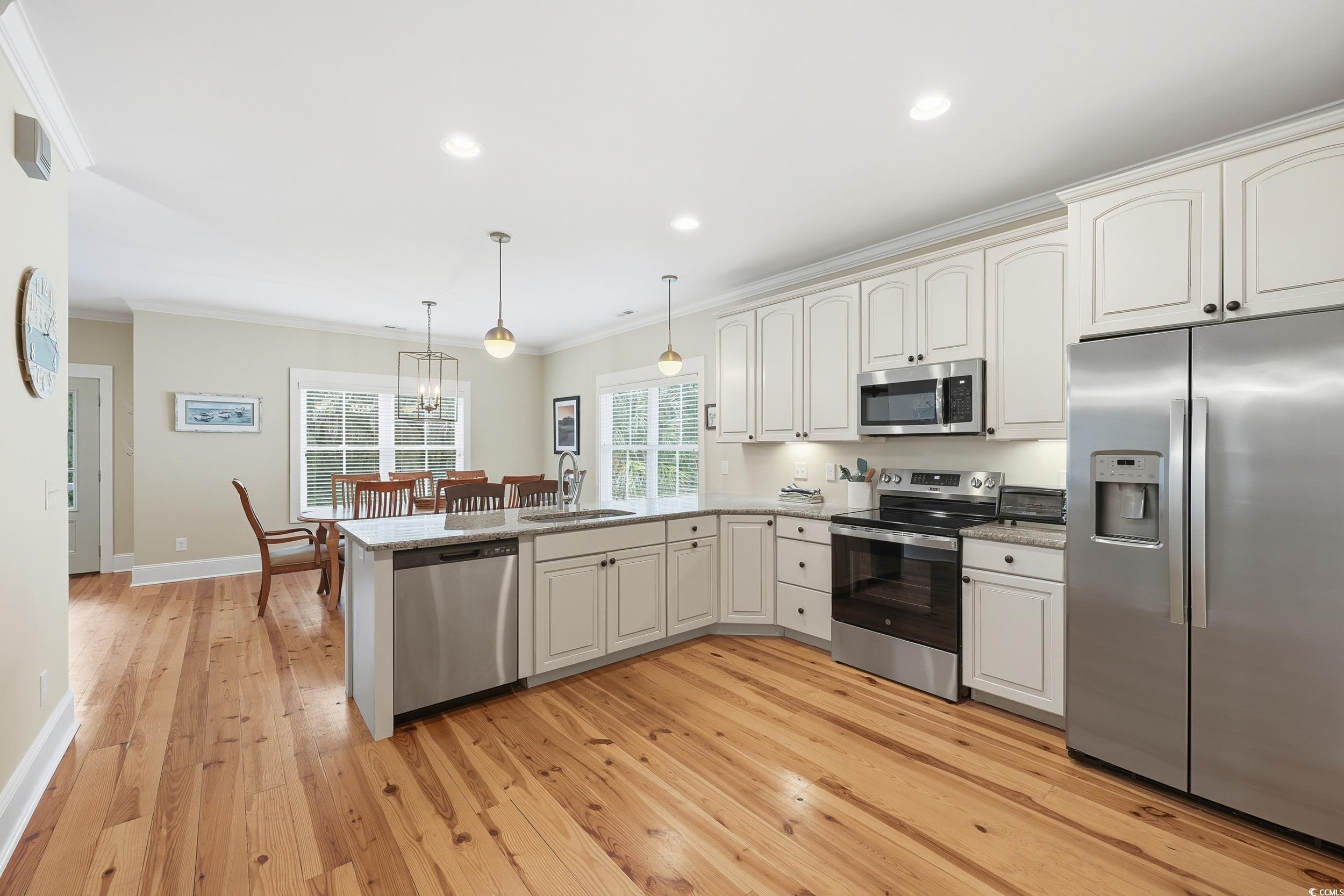 43 Sandlapper Way Pawleys Island, SC 29585 - Photo 8 of 33 Kitchen featuring appliances with stainless steel finishes, decorative light fixtures, crown molding, a peninsula, and light wood-style flooring