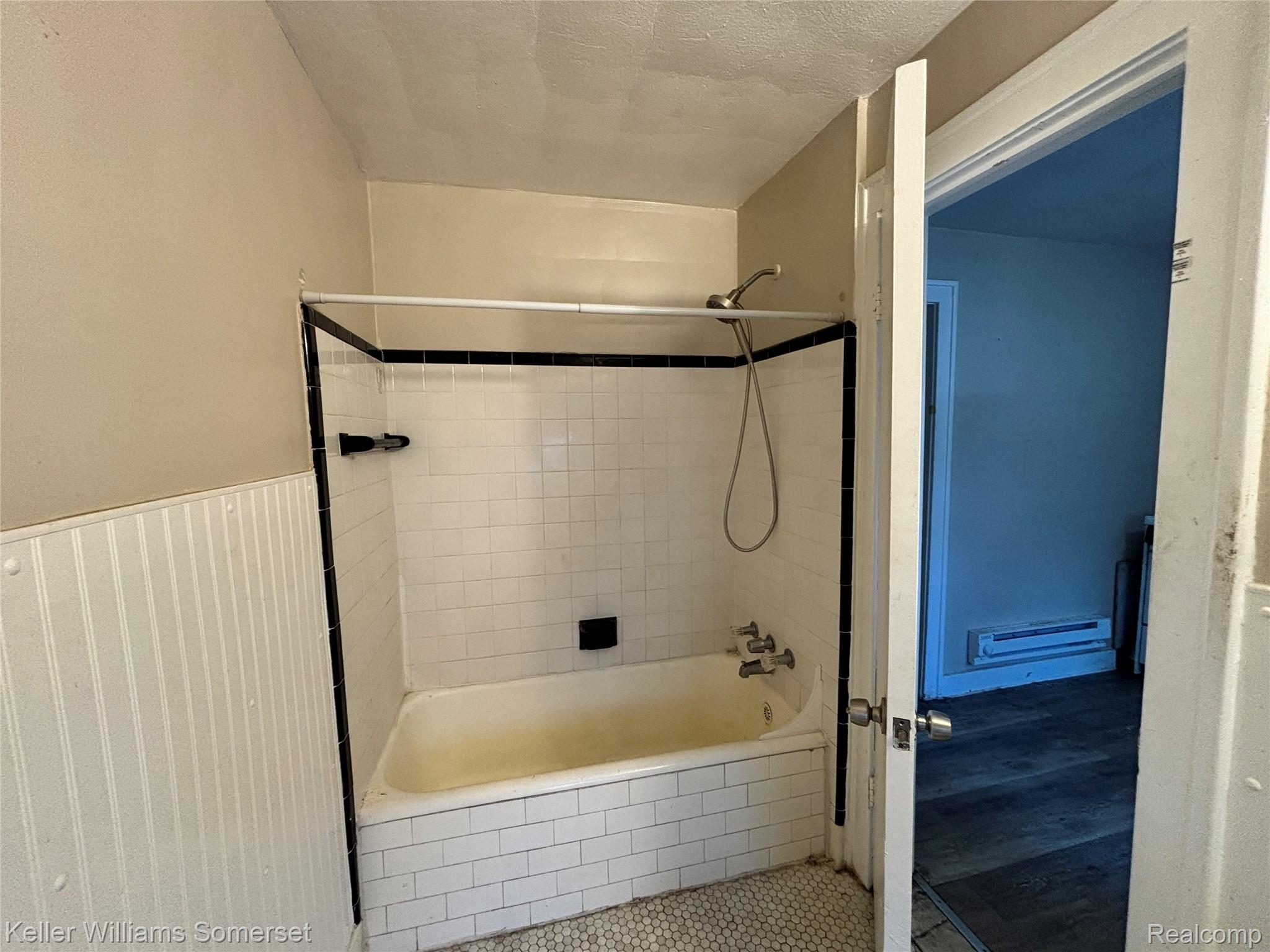 5783 Yorkshire Road Detroit, MI 48224 - Photo 5 of 13 Bathtub with white subway tile surround, black trim, and a handheld showerhead