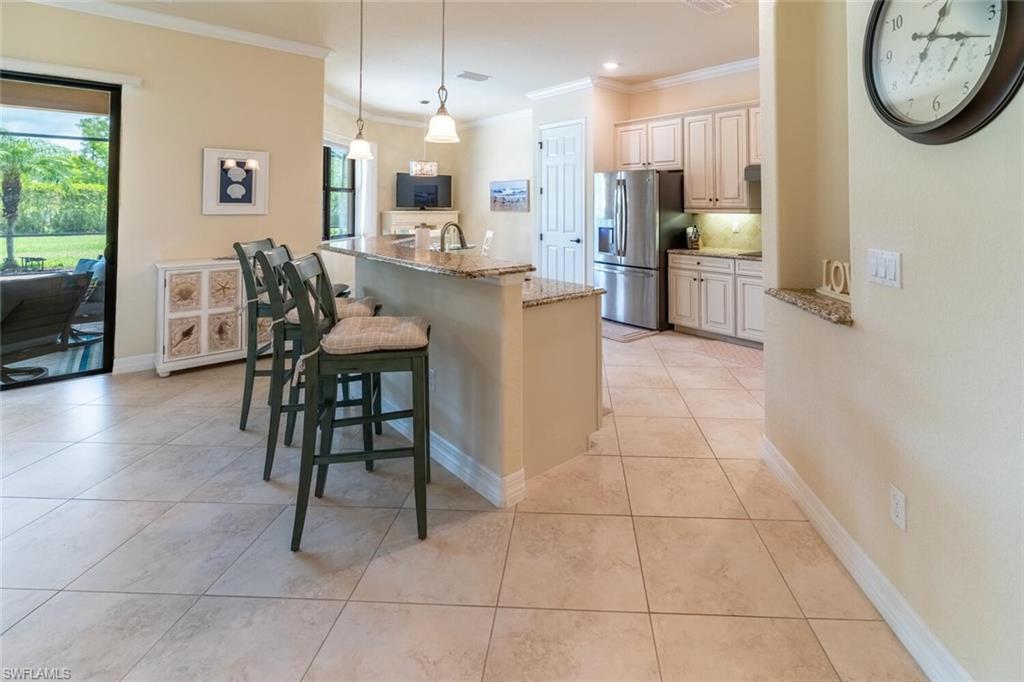9372 Vercelli Court Naples, FL 34113 - Photo 8 of 50 Kitchen with crown molding, stainless steel fridge with ice dispenser, a kitchen breakfast bar, light tile patterned flooring, and light stone counters