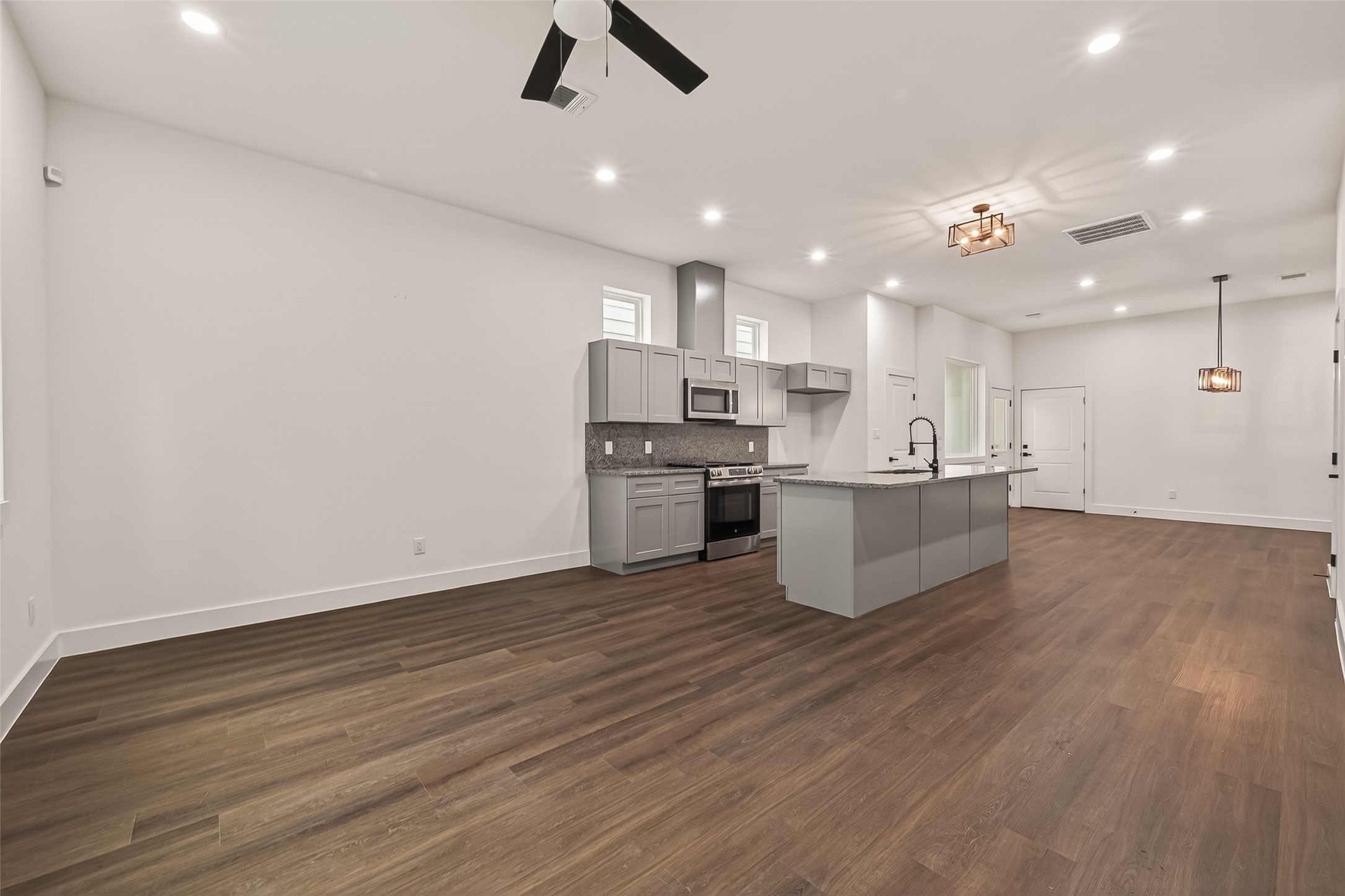 6808 Madrid Street Houston, TX 77021 - Photo 4 of 31 This photo showcases a spacious, open-concept living area with a modern kitchen featuring grey cabinets, stainless steel appliances, and a large island. The room has wood flooring, recessed lighting, and stylish ceiling fixtures, providing a clean and contemporary look.